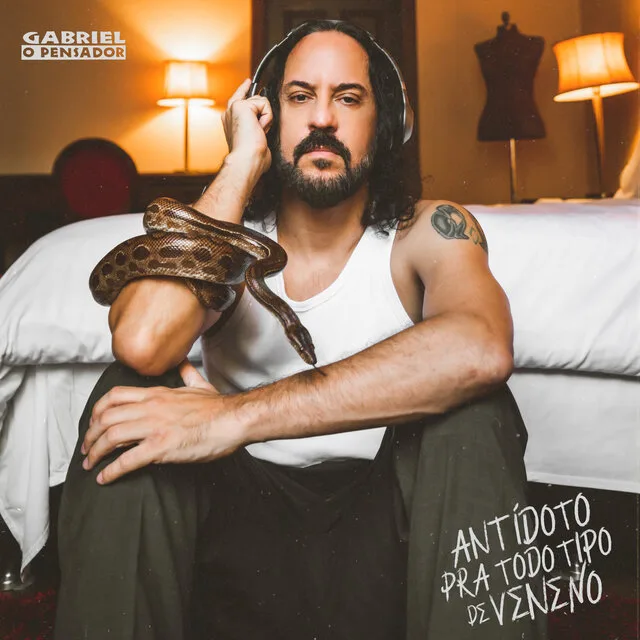 Gabriel o Pensador sentado em uma cama, calmamente com uma cobra enrolada no braço, demonstrando um vínculo único com a criatura.