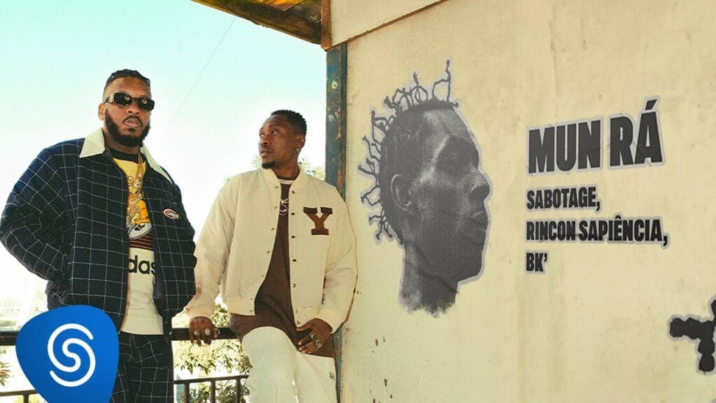 Rincon Sapiência e BK em frente a um mural com imagem do Sabotage e apresentação do clipe de Mun Rá.