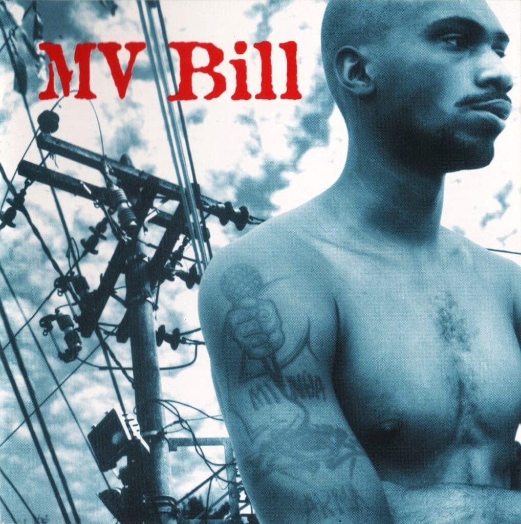Imagem 'azulada' de MV Bill sem camisa com destaque para a tatuagem de um microfone no seu braço direito; ao fundo uma estrutura de linha elétrica e um céu nublado, transmitindo uma atmosfera urbana.