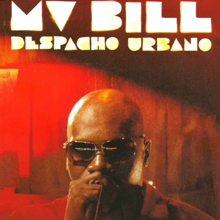 A capa do álbum 'Despacho Urbano' apresenta um close-up de MV Bill com óculos escuros contra um fundo vermelho com listras de luz verticais. Ele está segurando um microfone na boca, que está parcialmente visível. O texto 'MV BILL' está proeminentemente exibido em grandes letras brancas maiúsculas na parte superior, e abaixo dele, 'DESPACHO URBANO' está escrito em letras brancas maiúsculas menores.