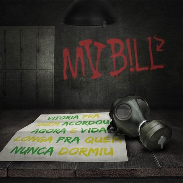 A imagem é a capa do álbum 'Vitória pra Quem Acordou Agora e Vida Longa pra Quem Nunca Dormiu', do MV Bill. A imagem é de um ambiente sombrio que se assemelha a um cômodo com armários de metal ao fundo, sugerindo um local industrial ou de vestiário. No centro, sobre uma mesa de madeira, repousa uma folha de papel dobrada com o título do álbum escrito em letras grandes e coloridas, alternando entre verde e amarelo, em referência às cores do Brasil. Ao lado do papel, uma máscara de gás escura adiciona um elemento de mistério e talvez perigo. Na parede de concreto atrás da mesa, o nome 'MV BILL' está pixado em vermelho transmitindo uma atmosfera urbana e de protesto. Uma luminária escura pendurada no teto ilumina a cena de forma sutil.