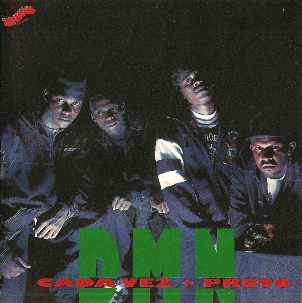 Capa do álbum 'Cada Vez Mais Preto' do grupo de rap DMN. Quatro homens negros estão posicionados lado a lado em um ambiente escuro, iluminados por uma luz frontal que destaca seus rostos e vestimentas. Xis, o terceiro homem, da esquerda para a direita, veste uma jaqueta da torcida organizada Gaviões da Fiel. Na parte inferior, as letras 'DMN' aparecem em tamanho grande e na cor verde, sobrepostas pelo título do álbum 'CADA VEZ + PRETO' em letras vermelhas menores. No canto superior esquerdo, encontra-se o logotipo vermelho da gravadora Zimbabwe Records.