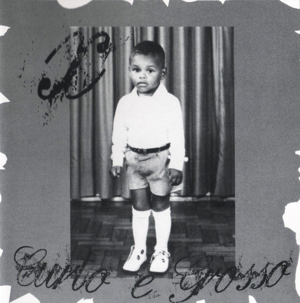 Uma imagem em preto e branco que serve como capa do álbum 'Curto e Grosso' do rapper X. No centro, há uma fotografia antiga de uma criança negra, vestindo uma camisa clara de mangas compridas, bermuda xadrez e meias brancas altas com sapatos claros. A criança está em pé diante de uma cortina listrada. A foto central é emoldurada por uma borda cinza texturizada com detalhes rasgados nas pontas. No canto superior esquerdo, há uma logomarca estilizada com a letra 'X' e, na parte inferior, o título 'Curto e Grosso' escrito em uma fonte cursiva elegante.