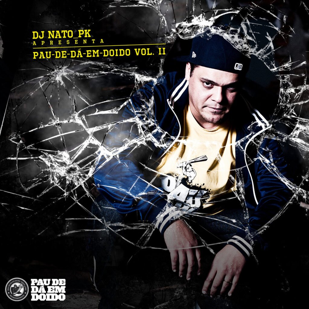 A imagem apresenta a capa do álbum Pau-de-Dá-em-Doido Vol. II, do respeitado produtor DJ Nato PK, exibindo o artista agachado sob um efeito visual de vidro estilhaçado que simboliza o impacto das batidas pesadas do Boom Bap brasileiro; com uma estética urbana crua em tons de azul e amarelo, a arte reforça o conceito de resistência do rap independente e a autoridade do DJ em reunir líricas afiadas sobre produções densas e autênticas.