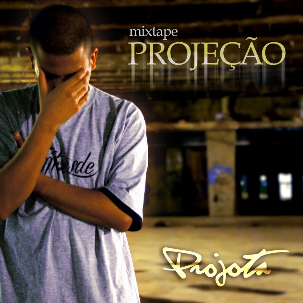 vaihiphop Gem personalizado vaihiphop disse A capa da mixtape 'Projeção' exibe o rapper Projota posicionado do lado esquerdo da imagem, enquadrado da cintura para cima. Ele veste uma camiseta cinza com gola e bordas das mangas na cor preta, contendo uma estampa escura no peito. O artista está de cabeça baixa, com a mão direita cobrindo o rosto e o braço esquerdo cruzado sobre o corpo. O cenário ao fundo é desfocado e revela um amplo espaço urbano vazio e rústico, semelhante a um galpão ou estacionamento, com piso de concreto, pilares e teto com vigas aparentes, iluminado por luzes amareladas. No canto superior direito, encontra-se a palavra 'mixtape' em letras minúsculas brancas e, logo abaixo, o título 'PROJEÇÃO' em letras maiúsculas e douradas com um leve efeito de brilho vertical. No canto inferior direito, o nome 'Projota' destaca-se em uma fonte cursiva grande, também na cor dourada.