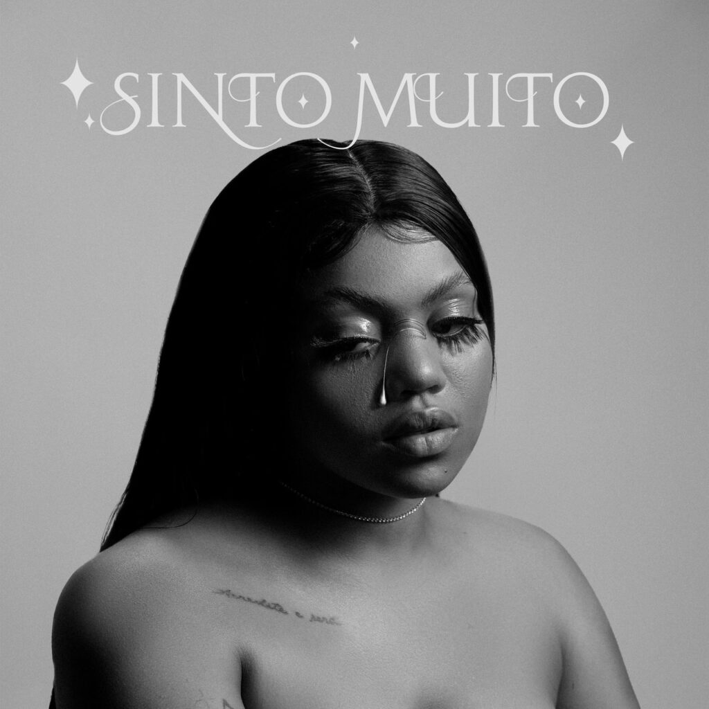 A capa do álbum 'Sinto Muito', da artista Duquesa, apresenta um retrato em preto e branco com uma carga emocional melancólica e sofisticada. A artista aparece em destaque, com o olhar baixo e desviado, exibindo uma maquiagem artística onde uma joia ou detalhe brilhante simula uma lágrima escorrendo de seu olho direito. Ela possui cabelos longos e lisos repartidos ao meio, usa cílios volumosos e uma gargantilha fina, deixando os ombros descobertos, onde se nota uma pequena tatuagem escrita na região da clavícula. No topo da imagem, o título 'SINTO MUITO' é escrito em uma fonte clássica e elegante, adornada por pequenos brilhos em formato de estrela de quatro pontas, sobre um fundo cinza neutro que reforça a atmosfera intimista e minimalista da obra.