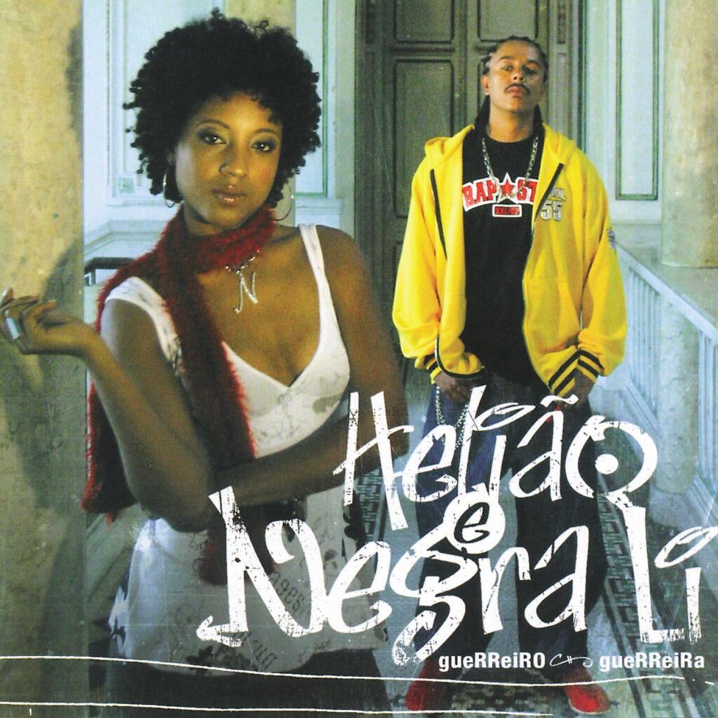 A capa do álbum, com estética urbana e do hip hop, apresenta dois artistas, Helião e Negra Li. Negra Li está em primeiro plano, à esquerda, usando uma blusa branca de alças e um cachecol vermelho peludo. Seu cabelo está no estilo black power e ela tem o olhar firme em direção à câmera. Atrás dela, à direita, Helião está com uma jaqueta de capuz amarela aberta, revelando uma camiseta preta com a logomarca da 'RAP SP'. 'Helião e Negra Li' está escrito em letras brancas estilizadas, imitando pichação ou giz, ocupando o centro e a parte inferior da imagem. Abaixo, lê-se 'gueRReiRO & gueRReiRa' em letras menores. Os artistas estão em um local que parece ser uma construção antiga, com colunas e uma porta de madeira ao fundo, e o piso é feito de ladrilhos geométricos.
