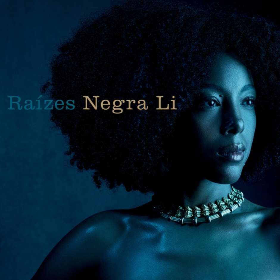 A capa do álbum Raízes, da cantora Negra Li, apresenta um retrato em close-up da artista em perfil três-quartos, iluminado por uma luz fria em tom azulado contra um fundo escuro. Seu cabelo volume black power emoldura a imagem e ela veste um colar rígido com detalhes esculpidos que envolve o pescoço. No lado esquerdo superior, o título do álbum, 'Raízes', e o nome da artista, 'Negra Li', estão escritos em uma fonte clássica com serifa em tom azul-claro.