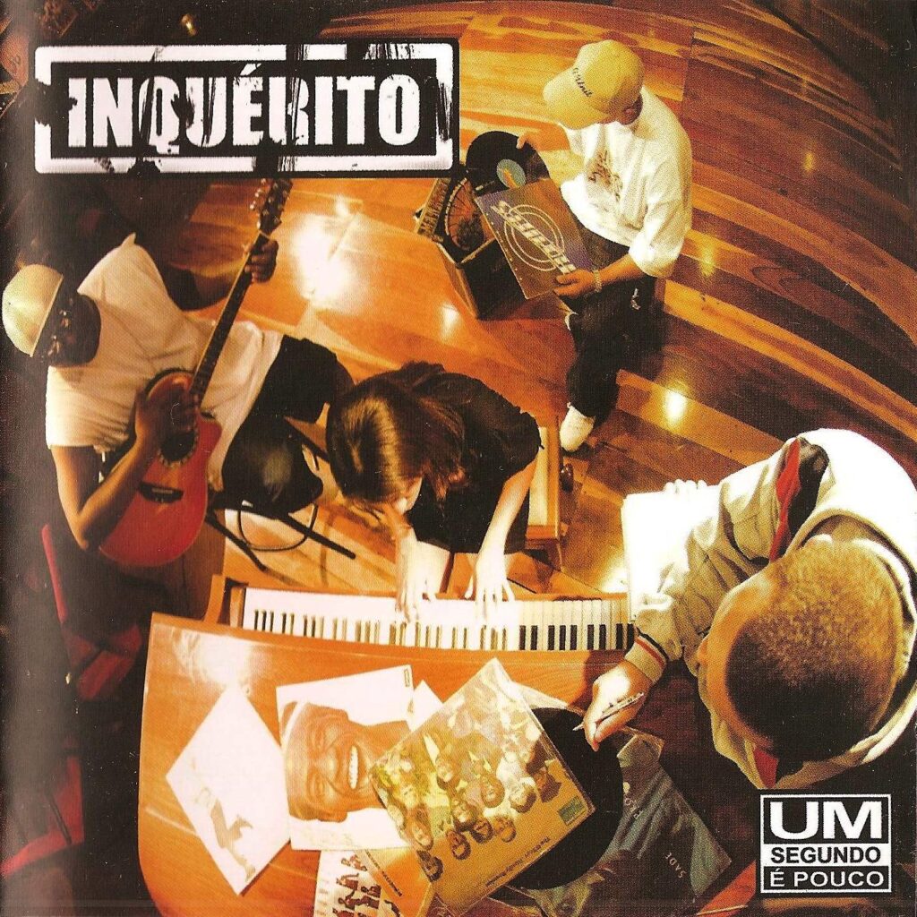A capa do álbum Um Segundo é Pouco, do grupo Inquérito, é vista de um ângulo superior (plongeant) mostrando os quatro integrantes em uma sala com piso de madeira, manuseando instrumentos musicais e discos de vinil. No canto superior esquerdo, o nome 'INQUÉRITO' está estampado em uma caixa retangular branca com letras vazadas e estilo desgastado. Distribuídos pela cena: no canto esquerdo, o integrante Pop Black veste camiseta branca e boné enquanto toca um violão de náilon vermelho; ao centro, Nicole aparece sentada tocando um piano de armário de madeira; no canto superior direito, o DJ Rodrigo, usando boné e camiseta branca, manuseia discos de vinil; e no canto inferior direito, Renan observa capas de discos de vinil espalhadas sobre a superfície do piano tocado por Nicole. No canto inferior direito, destaca-se um retângulo branco com o título do álbum em três linhas: 'UM', 'SEGUNDO' e 'É POUCO'.